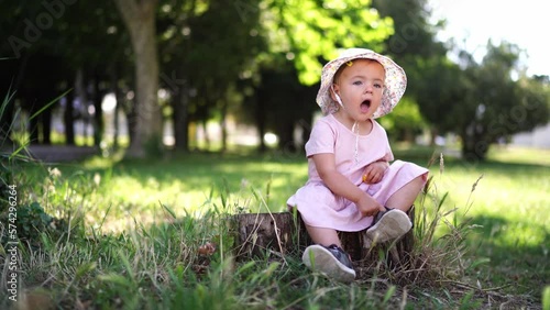 Little girl sits on a stump in a green park and sings photo