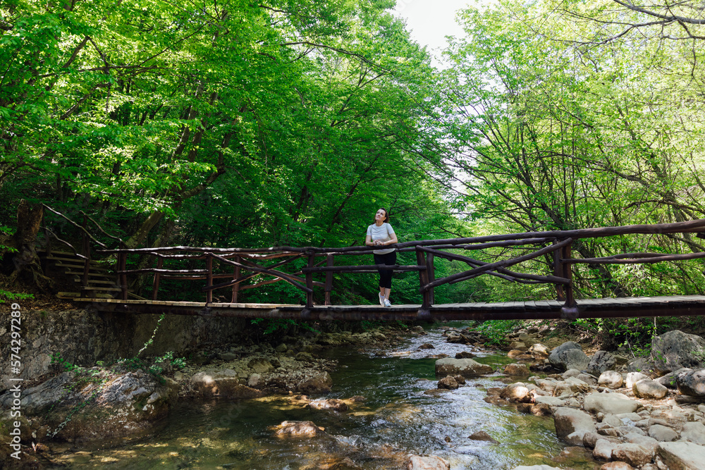 a woman stands on a bridge over a river in a green forest a woman stands on a bridge over a river in a green forest