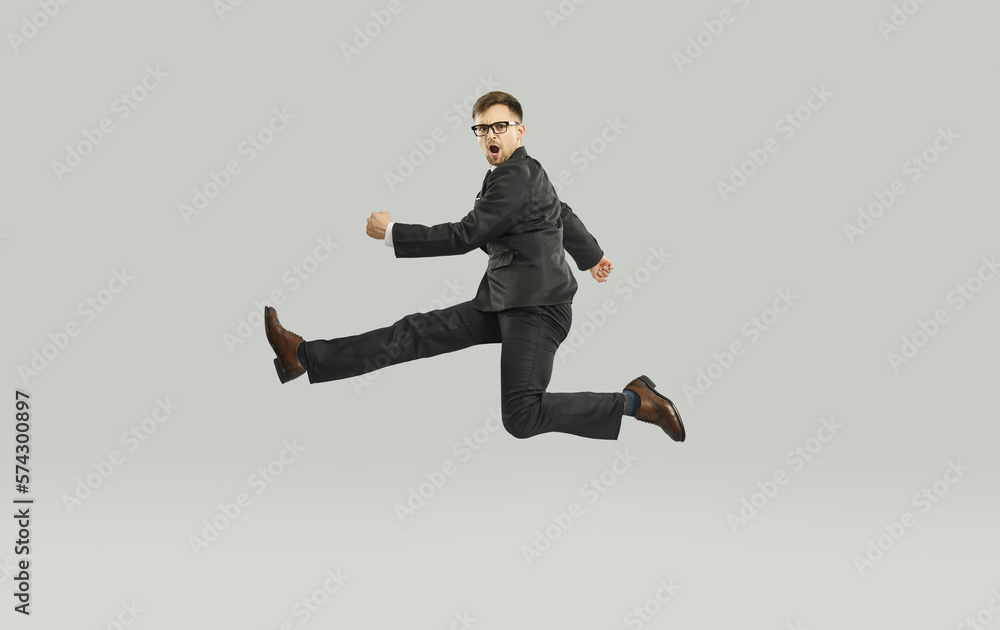 Businessman or office worker with lots of aggressive energy hurrying to work. Funny man in suit jumping high in air while running to business meeting. Full length, isolated on light gray background