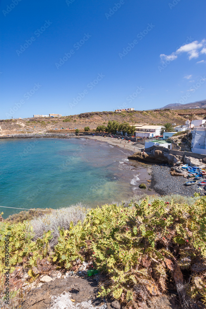 Views of the bay a beach with fishing village, with white houses. Tuneras in the foreground. Boats on the shore of the beach. Turquoise blue ocean. Yellow and brown hills in the background. In the bac