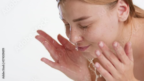 Medium close-up shot of attractive young slim Caucasian woman with long brown hair washes her face on white background | Clean face concept