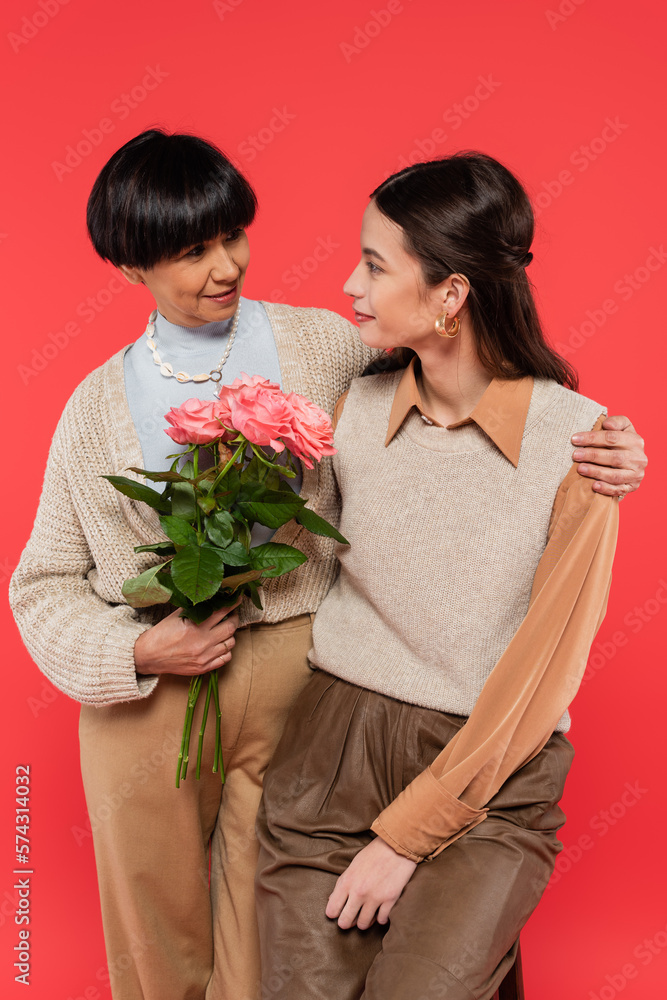 cheerful asian mother with bouquet of flowers hugging happy daughter isolated on coral cheerful asian mother with bouquet of flowers hugging happy daughter isolated on coral