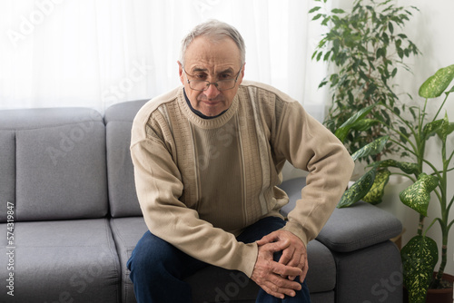 old man with his knee joint pain in sofa, pain in the elderly, health care, elderly care. Elderly man having a knee pain and sitting down. Grandfather with knee pain.