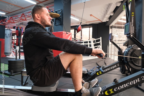 February 21, 2023 Ukraine, Dnipro. Rowing machine firm Concept 2. A man on a workout in the gym with his own weight. aeromagnetic simulator. Scandinavian traction for strength work of the back muscle