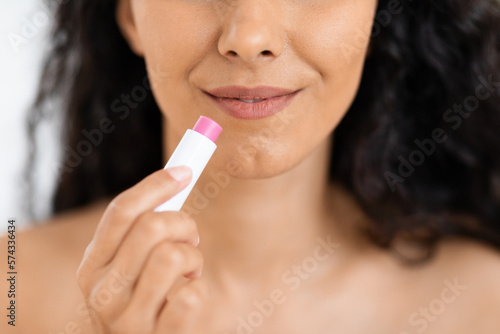 Happy millennial caucasian brunette lady with long hair uses moisturizing lipstick for makeup