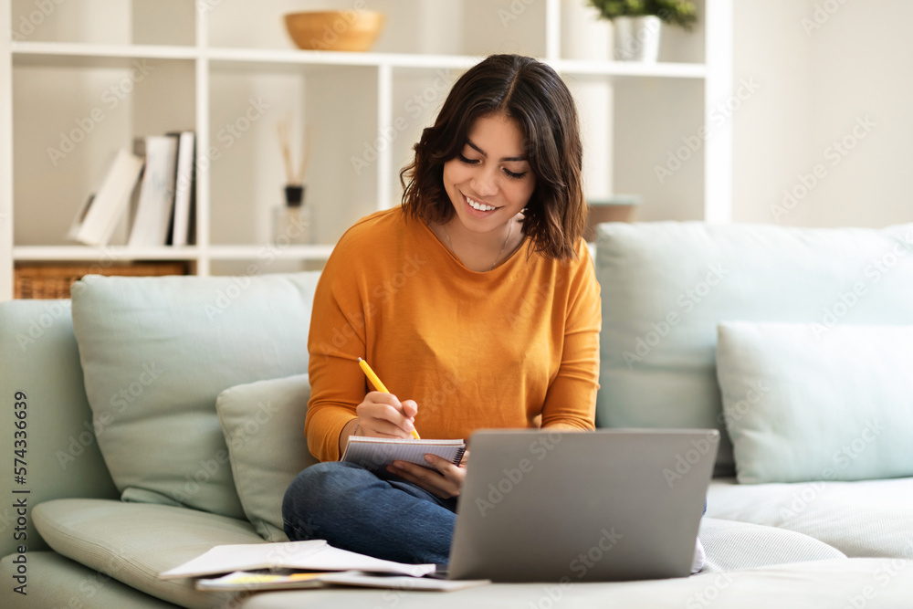 Young Smiling Arab Woman Taking Notes While Study With Laptop At Home Young Smiling Arab Woman Taking Notes While Study With Laptop At Home