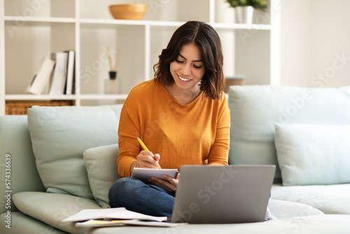 Young Smiling Arab Woman Taking Notes While Study With Laptop At Home