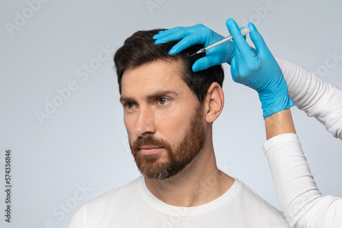 Middle aged man getting hair treatment at beauty salon, having mesotherapy session, grey background photo