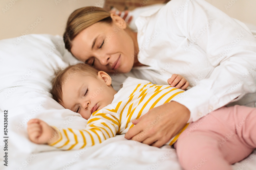 Peaceful mother and cute little child girl lying on bed, sleeping together, mom embracing daughter during daytime sleep