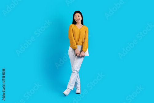 Happy young asian woman with laptop posing on blue