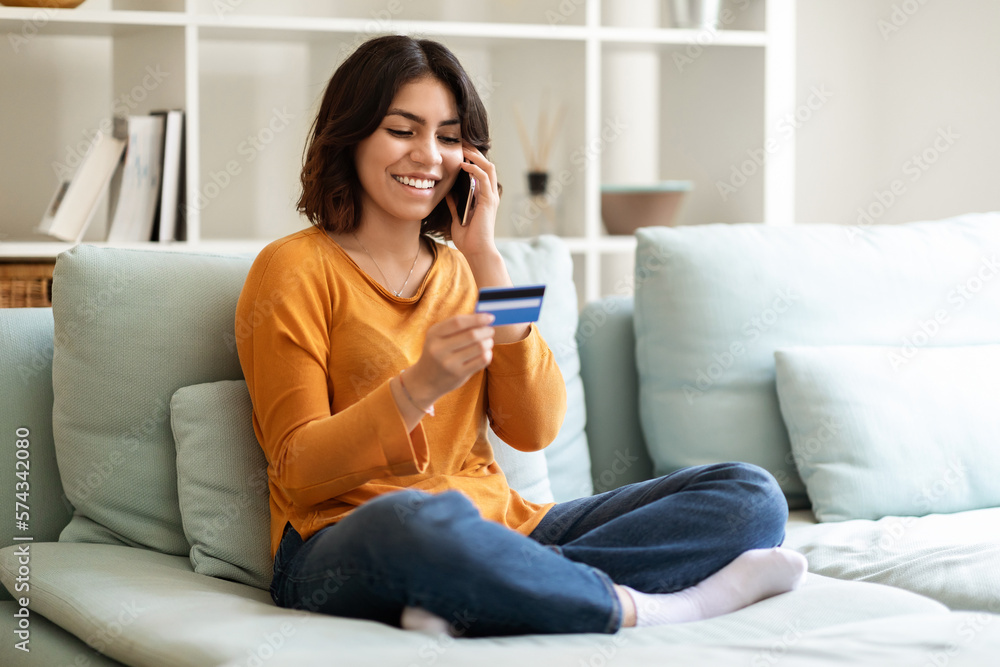Young Smiling Arab Woman Holding Credit Card And Talking On Mobile Phone Young Smiling Arab Woman Holding Credit Card And Talking On Mobile Phone