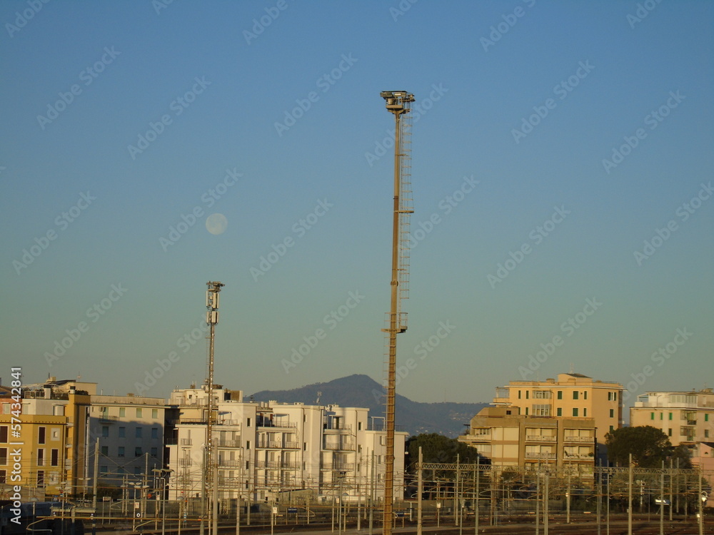 Sestri Levante, Italy - February 07, 2023: Almost full moonlight over the station of Sestri in winter days. Beautiful sunset hidden behind the mountains. Moon over the city by day. Sestri Levante, Italy - February 07, 2023: Almost full moonlight over the station of Sestri in winter days. Beautiful sunset hidden behind the mountains. Moon over the city by day.