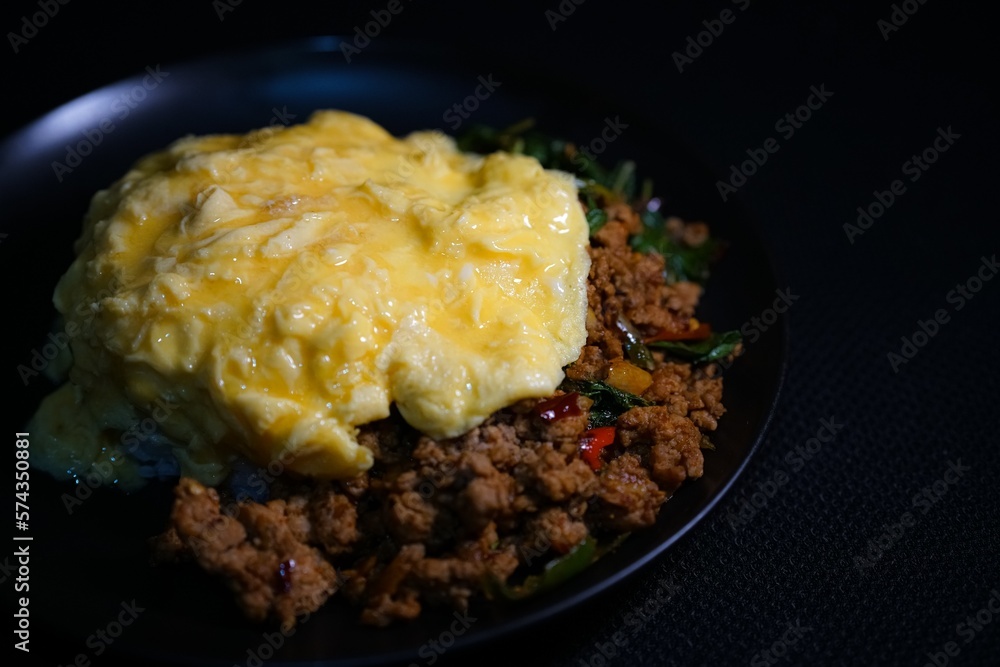 Close up Stir-fried basil with minced pork and scrambled eggs in a black plate on a black background. Close up Stir-fried basil with minced pork and scrambled eggs in a black plate on a black background.