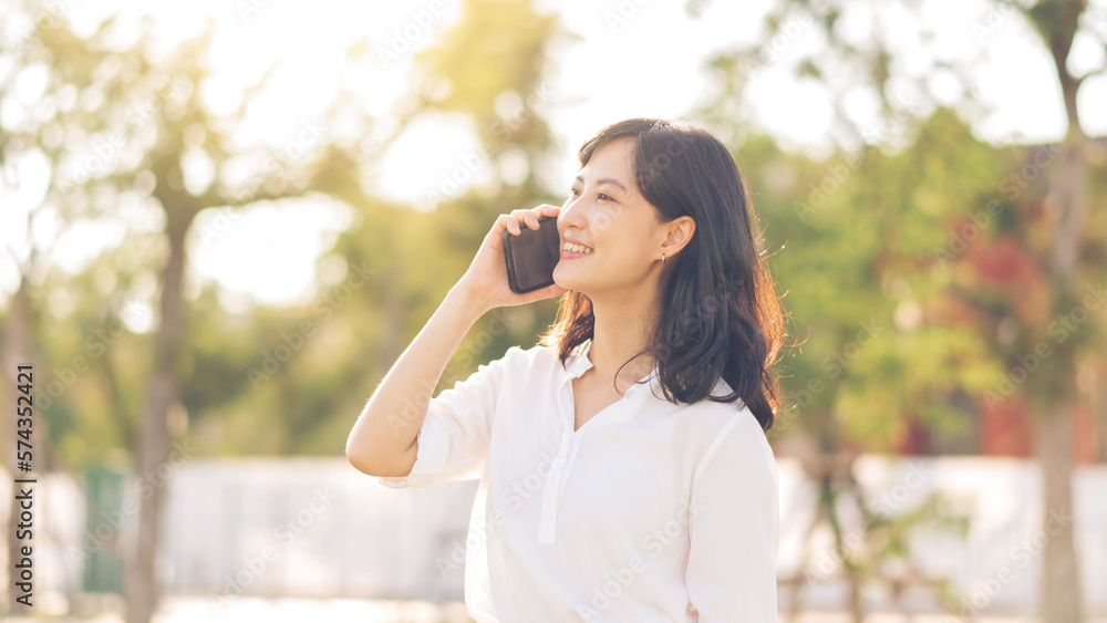 Portrait beautiful young asian woman with smart mobile phone around outdoor nature view in a sunny summer day Portrait beautiful young asian woman with smart mobile phone around outdoor nature view in a sunny summer day