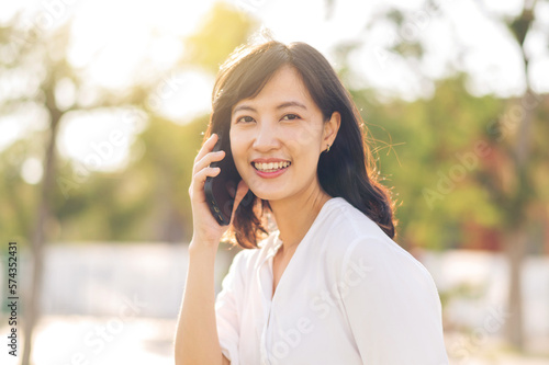 Portrait beautiful young asian woman with smart mobile phone around outdoor nature view in a sunny summer day