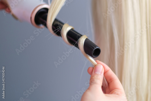 woman makes curls hairstyle with curling iron. Long light blond natural hair