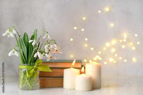 Bouquet of Snowdrop flowers   books and candles on table  abstract blurred light background. symbol of spring season. Relaxation  reading time  harmony of nature.