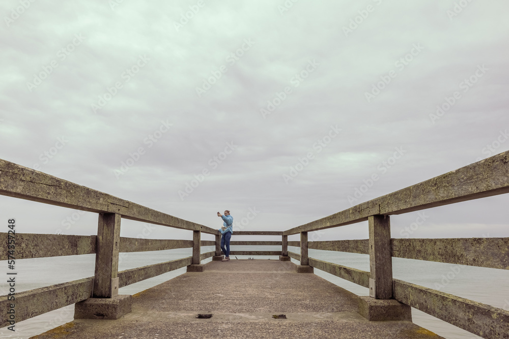 Fototapeta premium two girls are standing in jackets on a bridge in the distance and taking pictures on the phone, there is a place for an inscription beautiful sea landscape