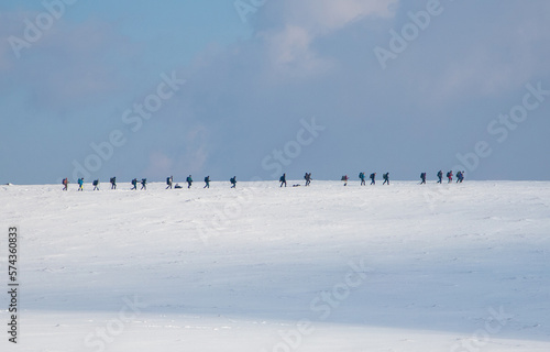 Many tourists walking in a row on a field with snow