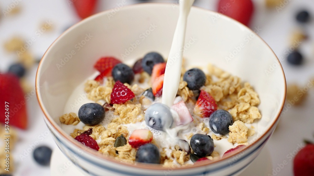 Milk pouring in bowl of healthy breakfast crunchy Granola Cereals with stawberry , blueberry vegan food, clean eating, dieting concept Milk pouring in bowl of healthy breakfast crunchy Granola Cereals with stawberry , blueberry vegan food, clean eating, dieting concept
