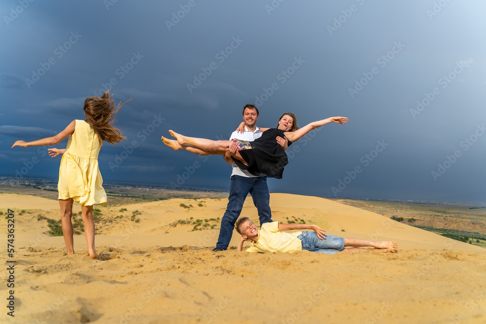 Happy family of mother, father, daughter and son jumping, laughing and having fun in sand dunes on vacations. Happy family of four jumping on high sand dune at mountains Happy family of mother, father, daughter and son jumping, laughing and having fun in sand dunes on vacations. Happy family of four jumping on high sand dune at mountains