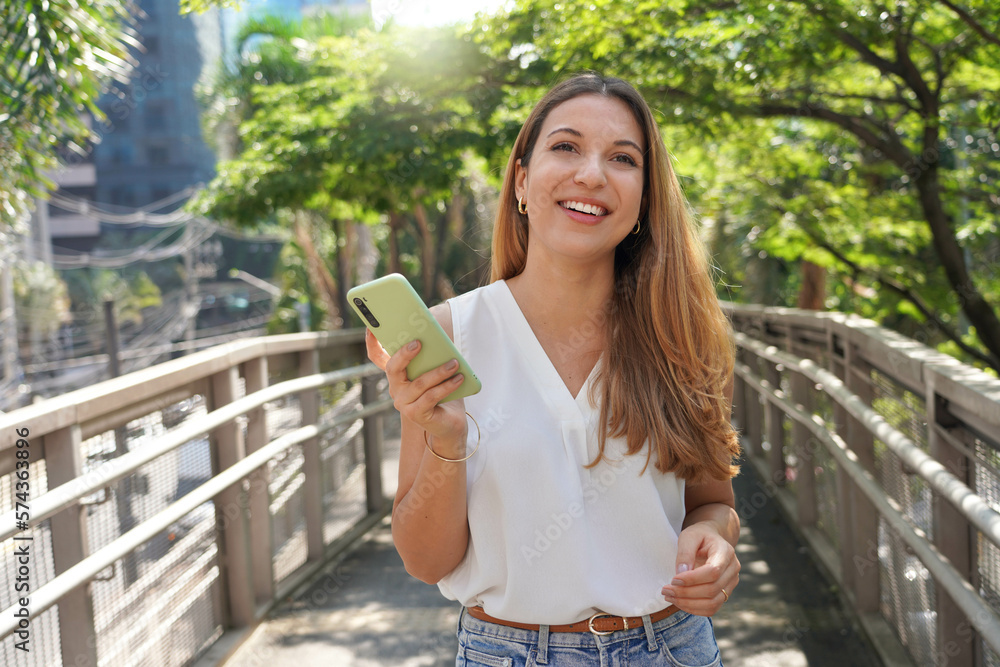 Attractive Brazilian female entrepreneur walking in Sao Paulo sustainable metropolis holding a smartphone