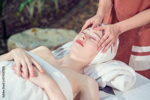 Beautiful caucasian young woman lying on bed with facial massage therapist on forehead doing facial massage, moisturizing facial spa and beautiful white skin relaxing in spa salon