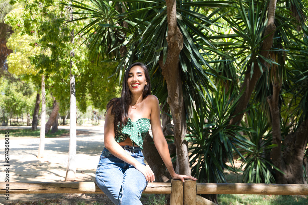 Beautiful woman with black hair leaning on a wooden railing in the park. The woman is doing different body postures while posing for photos. Autumn and nature concept. Beautiful woman with black hair leaning on a wooden railing in the park. The woman is doing different body postures while posing for photos. Autumn and nature concept.