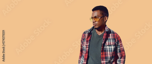 Portrait of stylish african man wearing sunglasses, red plaid shirt, guy looking away isolated on brown background, blank copy space for advertising text
