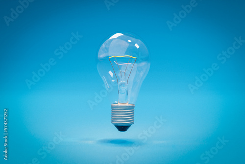 single glass lightbulb with filament wire floating in the air over infinite blue background; 3D Illustration