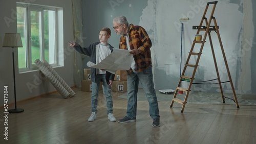 Grandpa and grandson are looking through sheet with plan of an apartment and discussing renovation project. Elderly man and young boy are planning the improvement of their home. Concept of repair