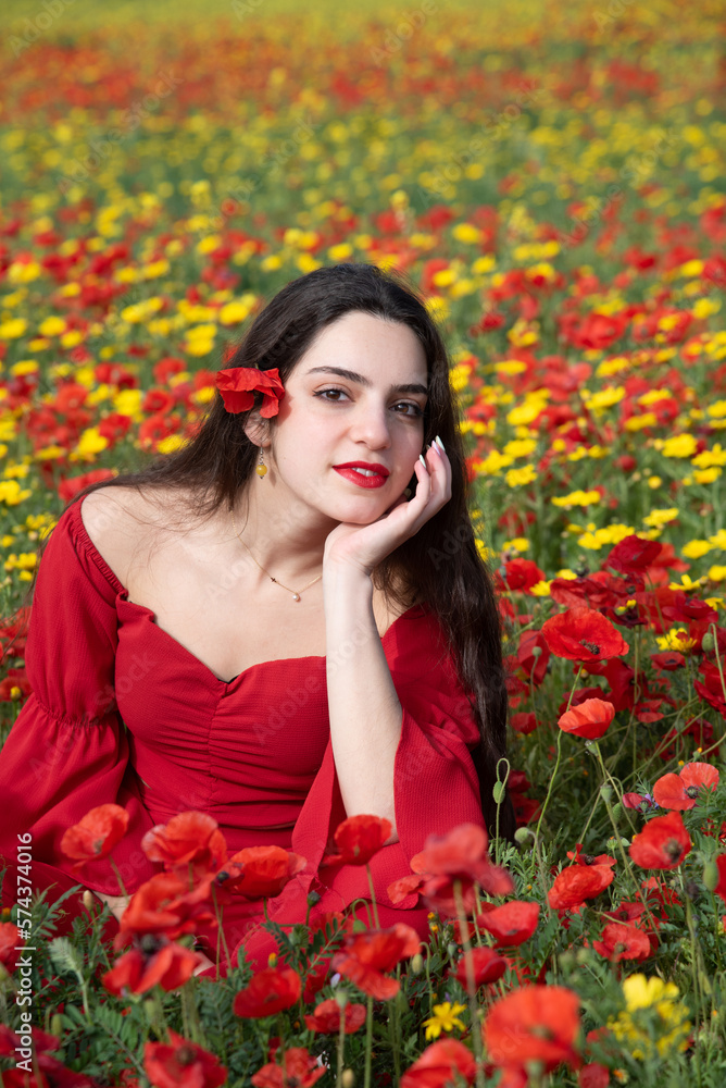 Naklejka premium Portrait of a young woman dressed in red smiling in the field of red poppies in spring. Springtime blooming season