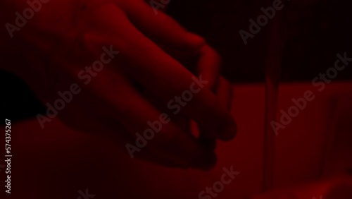 Hands of a maniac killer wash away the blood in the sink in the illumination of a police flasher. Slow motion.
