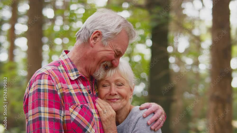 Loving senior couple hugging on walk through woodland countryside enjoying peace and beauty of nature- shot in slow motion Loving senior couple hugging on walk through woodland countryside enjoying peace and beauty of nature- shot in slow motion