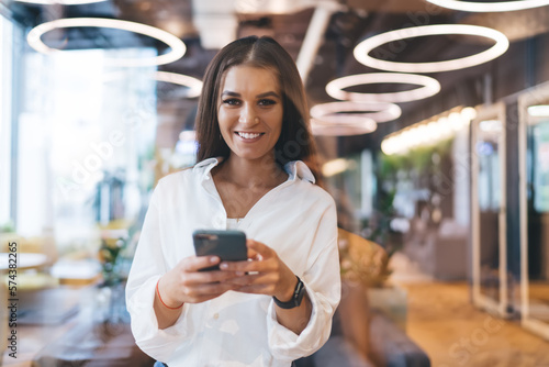 Smiling woman using smartphone while standing in cafe