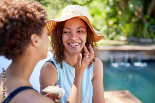 Happy, playful lesbian couple applying sunscreen to nose at poolside photo