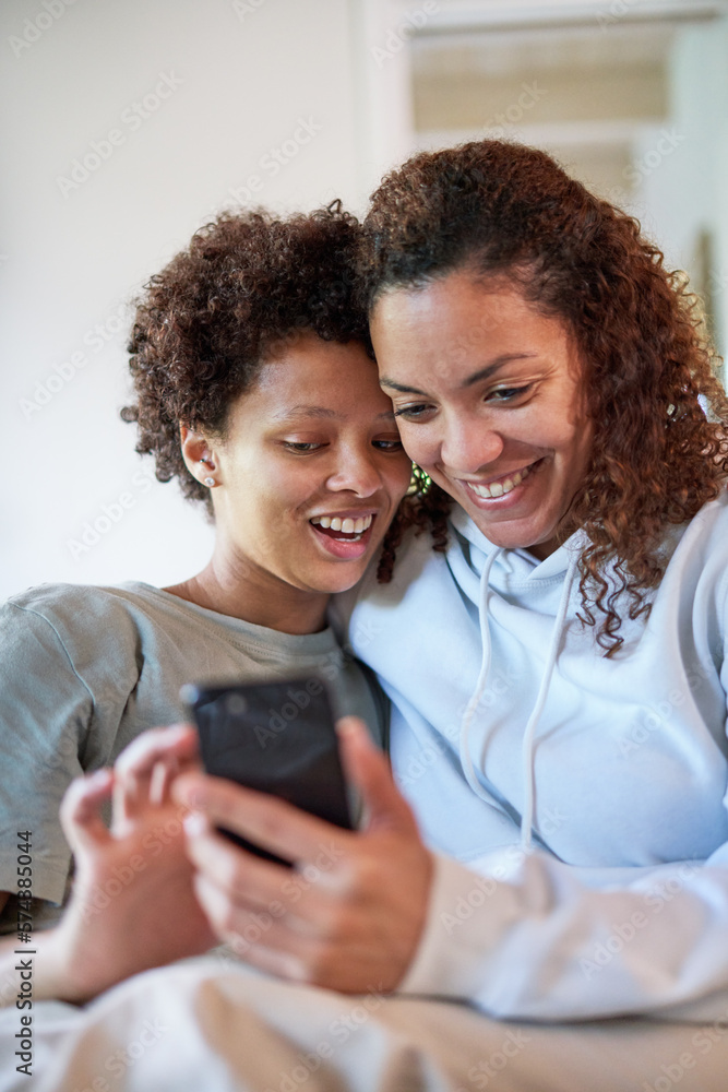 Happy lesbian couple using smart phone together at home Happy lesbian couple using smart phone together at home