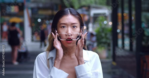 Amazed asian female shocked, look at camera takes off glasses. Portrait of asian woman in glasses, amazed by what she see and smiling with braces, standing at city mall photo