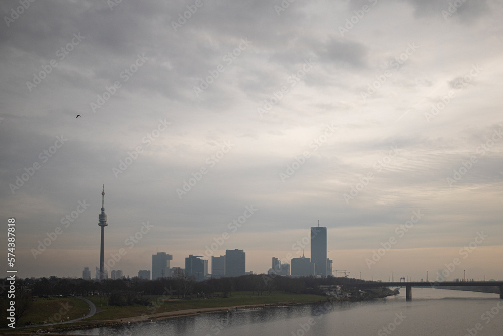 Photograph of the TV tower and Danube river in Donaustadt district, Vienna, Austria and a raven flying during a cloudy day.