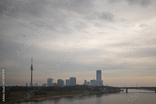 Photograph of the TV tower and Danube river in Donaustadt district, Vienna, Austria and a raven flying during a cloudy day. © Estefania