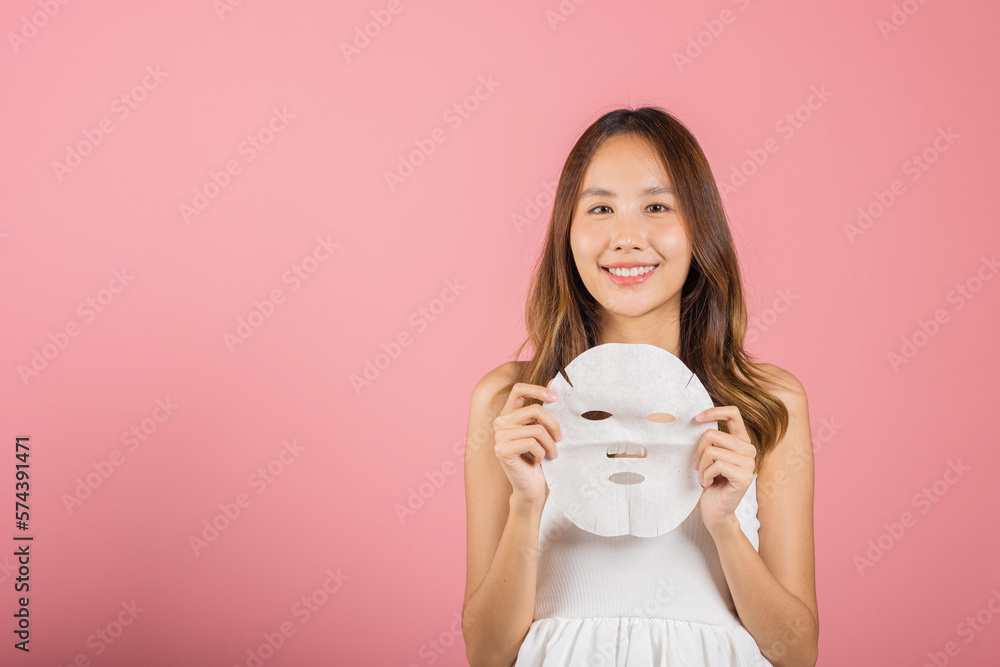 Healthcare spa. Asian woman holding purifying mask face on hands, Portrait beautiful female smiling holds facial sheet mask, Studio shot isolated on blue background, Face care and beauty treatments Healthcare spa. Asian woman holding purifying mask face on hands, Portrait beautiful female smiling holds facial sheet mask, Studio shot isolated on blue background, Face care and beauty treatments