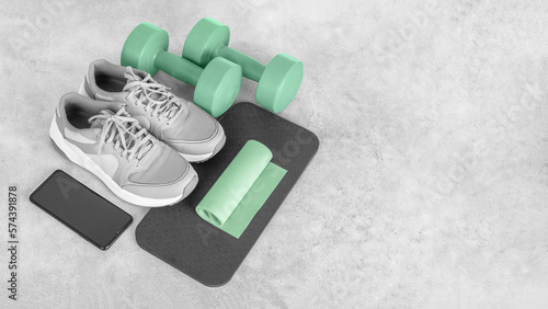 Fitness equipment on a gray concrete background. Sports shoes, smartphone, dumbbells, mat, exercise band, copy space. Fitness and activity. Smart fitness training. Home workout online. 