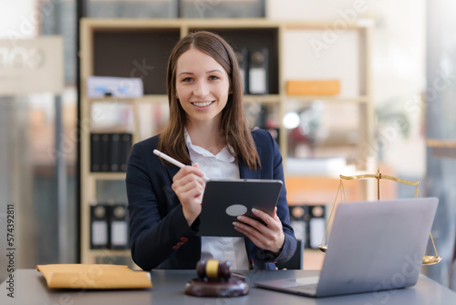 Female lawyer sitting happily working on laptop computer with hammer and legal book scales.