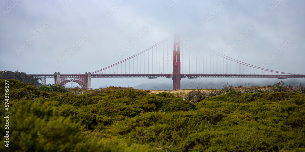 Fototapeta premium panorama of the golden gate bridge in san francisco during foggy weather; the famous red bridge emerging from behind the clouds, gloomy photo of the golden gate bridge