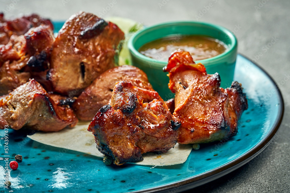 Grilled pork shish kebab in a blue plate with sauce and pita bread. Close-up.