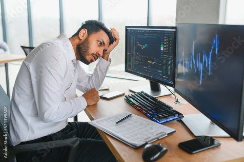 Portrait of a positive successful Indian or Arabian trader, stock market broker, Crypto charts on laptop screen