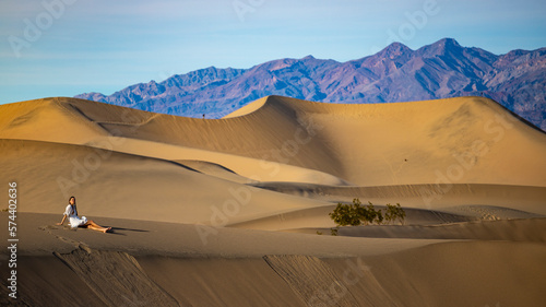 girl in white dress sits and relax on large sand dunes in mesquite flat sand dunes in death valley national park. Roadtrip in California, USA