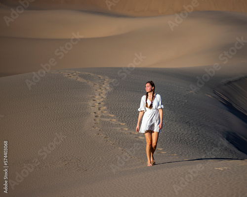 beautiful girl in lace dress lost in the middle of sandy desert; walking through mesquite flat sand dunes at sunset photo