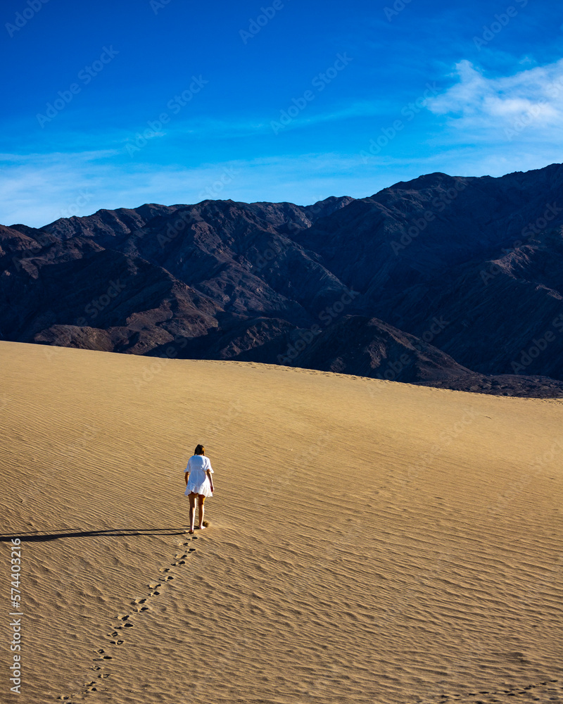 Beautiful girl in white dress walk on large, vast and stunning Mesquite Flat Sand Dunes in Death Valley National Park, California State, USA. 