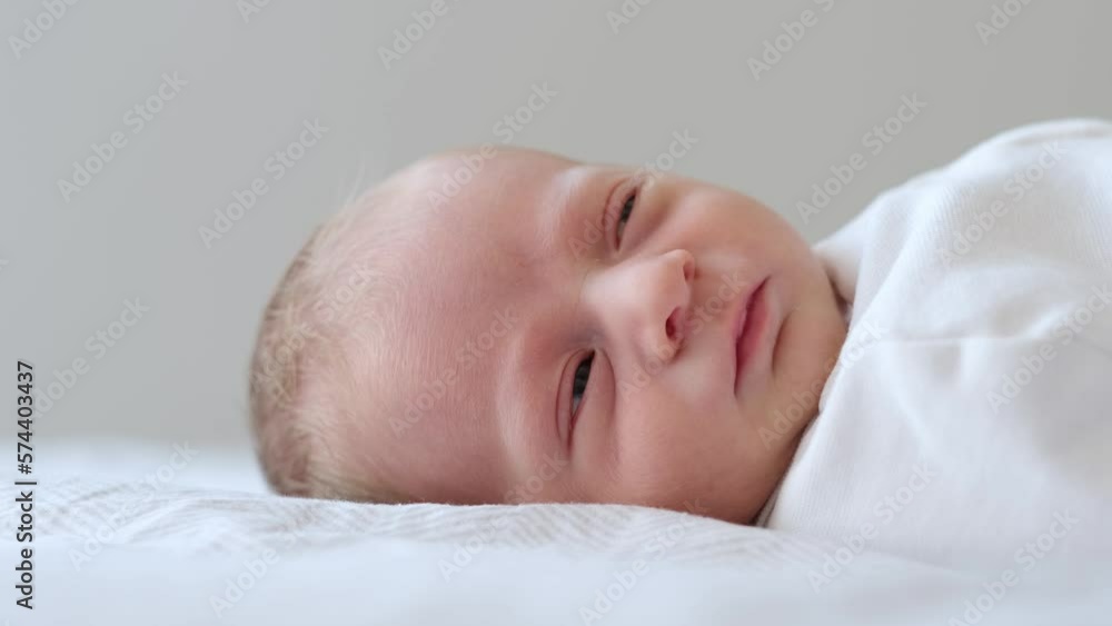 Close-up of cute adorable newborn baby boy few days old lying on back on white bed at home opening eyes. Purity,innosence concept. Close-up of cute adorable newborn baby boy few days old lying on back on white bed at home opening eyes. Purity,innosence concept.